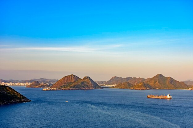 Foto buque de carga llegando a la bahía de guanabara en río de janeiro con la ciudad de niteroi en el fondo por la tarde