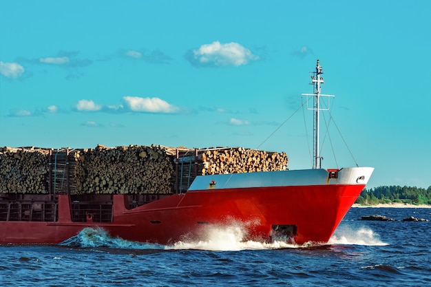 Buque de carga rojo completamente cargado con madera en movimiento en días claros