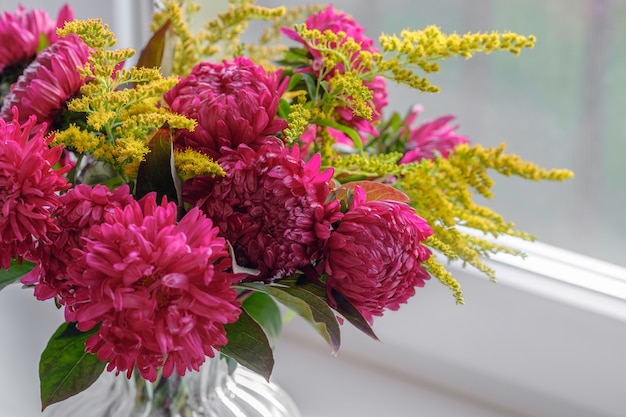 Buquê de dálias magenta. Rosa fresca roxa do grupo com as rosas amarelas das peônias flor em um vaso de vidro no peitoril da janela