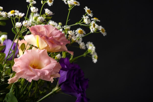 Buquê de eustoma com buxo e galhos de folhas pequenas em uma mesa em um fundo preto