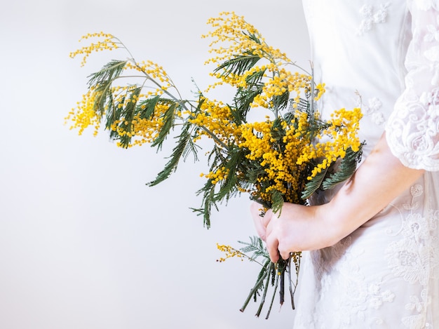 Buquê de flores amarelas e brilhantes nas mãos de uma jovem com um vestido branco. isolado, close up.