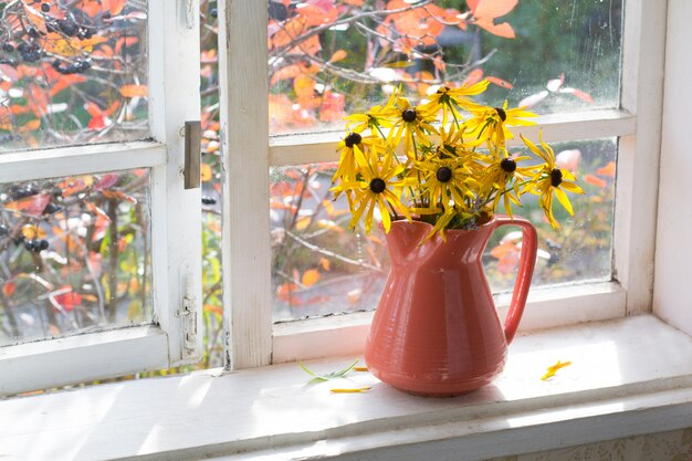 buquê de flores amarelas em um vaso no peitoril da janela