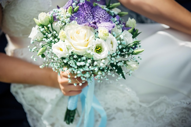 Buquê de flores brancas e lilás nas mãos de uma jovem noiva, close-up. imagem horizontal, foco seletivo. conceito de dia de casamento feliz.