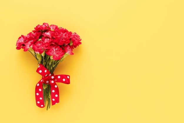 Buquê de flores de cravo vermelho decorado com fita com um laço em um fundo amarelo brilhante