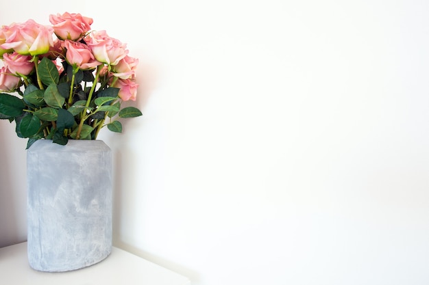 Buquê de flores de lindas rosas em um vaso moderno de concreto perto de fundo branco, espaço para texto