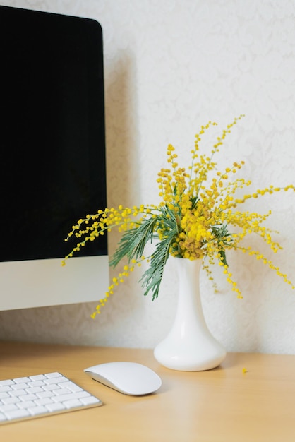 Buquê de flores de mimosa amarelas em um vaso em uma área de trabalho com um computador