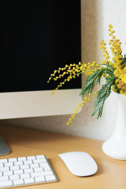 Buquê de flores de mimosa amarelas em um vaso em uma área de trabalho com um computador