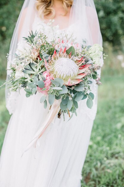 Buquê de flores de protea, suculentas e ramos de eucalipto nas mãos da noiva.