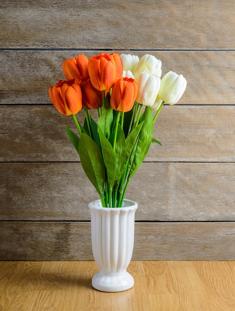 Buquê de flores de tulipa laranja, branco em um vaso no chão de madeira