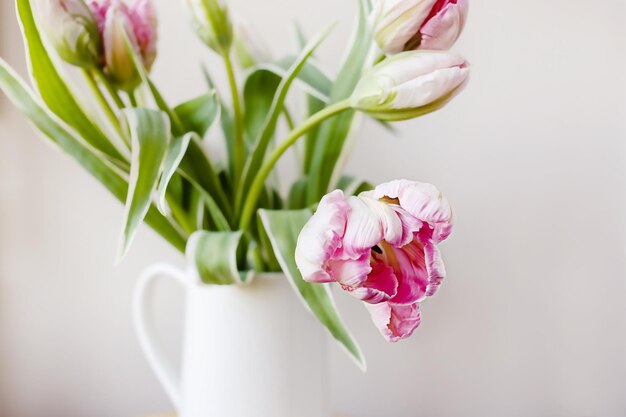 Buquê de flores de tulipa rosa com caules frescos verdes em um vaso de porcelana branca em uma moldura de janela branca com fundo de céu azul Ideia de decoração floral de botânica colorida vibrante