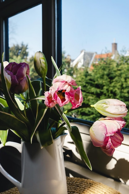 Buquê de flores de tulipa rosa com caules frescos verdes em um vaso de porcelana branca em uma moldura de janela branca com fundo de céu azul Ideia de decoração floral de botânica colorida vibrante