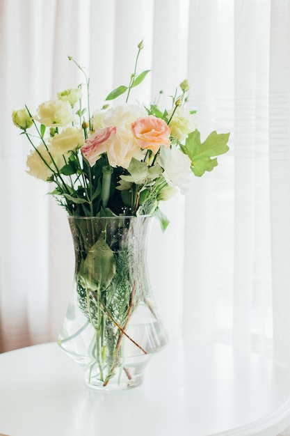 Buquê de flores em um vaso transparente sobre a mesa no contexto da janela