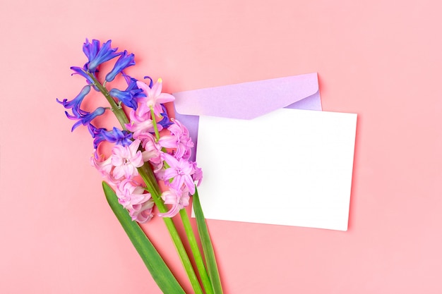 Buquê de flores jacintos, envelope lilás e papel branco nota na mesa-de-rosa