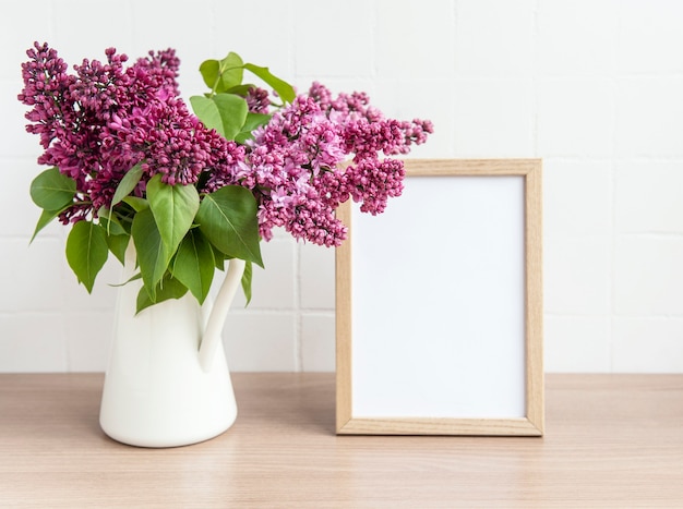 Buquê de flores lilás em um vaso e moldura vazia em uma mesa de madeira.