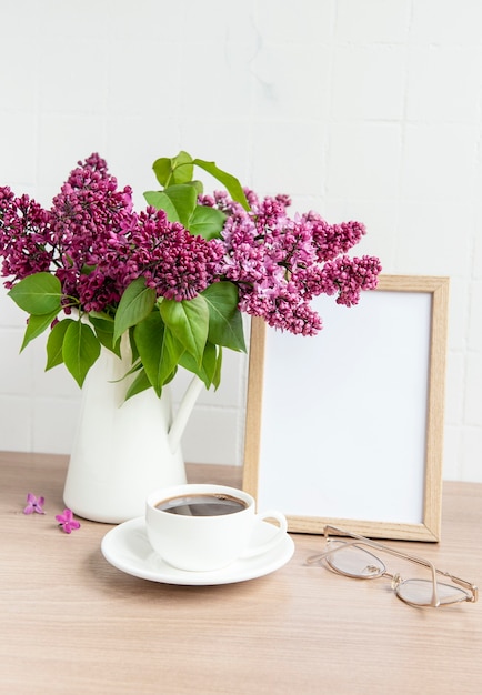 Buquê de flores lilás em um vaso e moldura vazia em uma mesa de madeira.