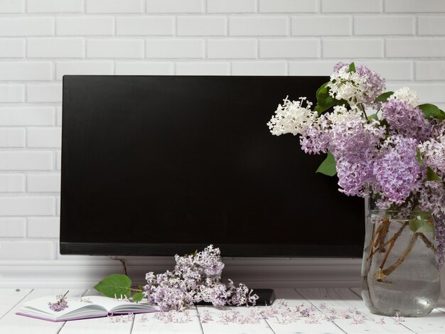 Buquê de flores lilás em vaso de vidro, caderno aberto, tela de monitor preta, espaço de trabalho de primavera