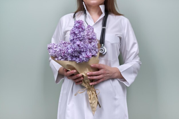 Buquê de flores lilás nas mãos da médica com estetoscópio. Dia mundial da saúde, enfermeira feliz com flores sobre fundo verde