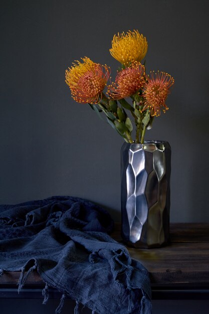 Buquê de flores protea exóticas amarelas e laranja em um vaso de metal em um fundo escuro