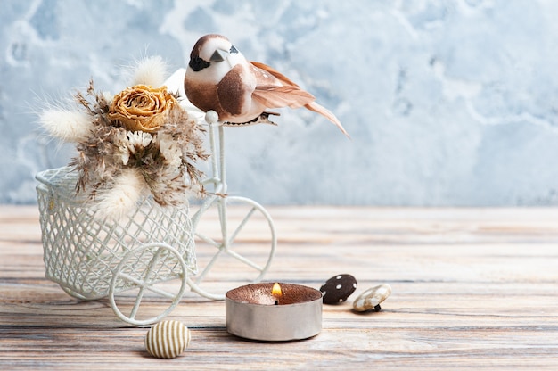 Buquê de flores secas em bicicleta decorativa com pequeno pássaro marrom e uma vela acesa na mesa. Cartão de felicitações para casamento ou feriado em tons naturais com espaço de cópia