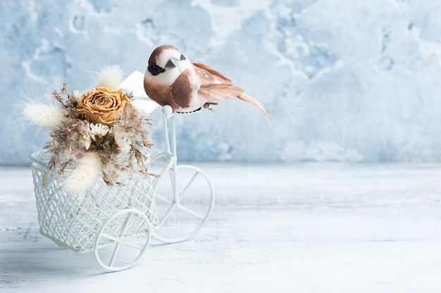 Buquê de flores secas na bicicleta decorativa com pequeno pássaro marrom em cima da mesa. Cartão de felicitações para casamento ou feriado em tons naturais com cópia, espaço