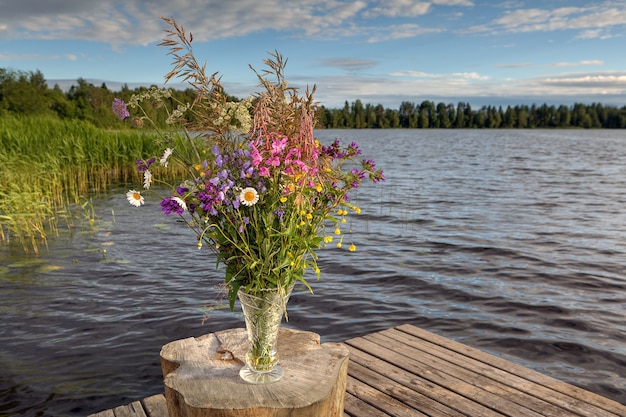 Buquê de flores silvestres em um vaso de cristal do lago da floresta.