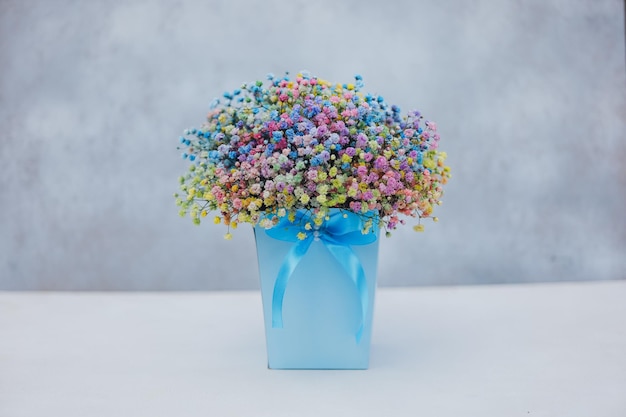 Buquê de gypsophila multicolorido em uma caixa azul com um laço em um fundo cinza