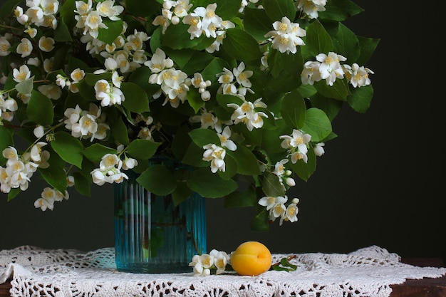 Buquê de jasmim em uma jarra de vidro e um damasco na mesa de flores brancas