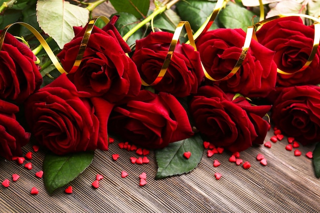 Buquê de lindas rosas vermelhas com pequenos corações na mesa de madeira closeup