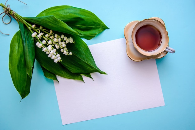 Foto buquê de lírios do vale, uma xícara de chá e uma folha de papel