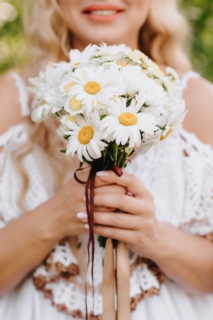 Foto buquê de margaridas nas mãos da noiva no fundo de um vestido branco