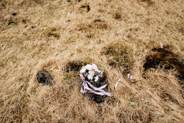 Buquê de noiva de rosas brancas brunia e leucadendron no chão em grama seca na Islândia