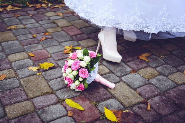 buquê de noivas no chão ao lado de sapatos e vestidos e folhas de outono