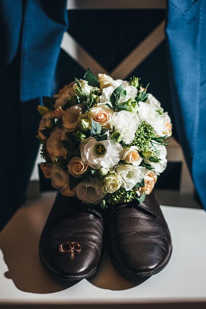 Buquê de noivos de sapatos masculinos e anéis em um conceito de pedestal branco para agência de eventos