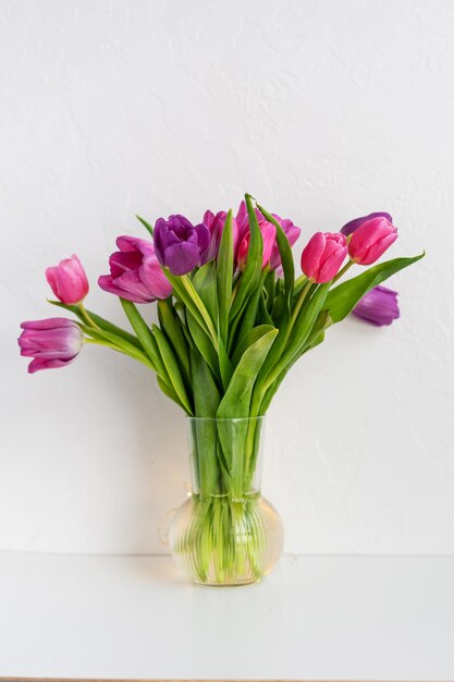 Buquê de primavera de flores de tulipas vermelhas e rosa no vaso de vidro sobre a mesa de madeira