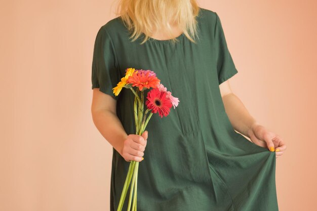 Buquê de primavera de gerberas nas mãos da mulher em fundo bege claro Retrato de mulher jovem e bonita segurando uma gerberas em interiores claros