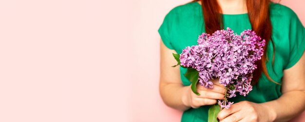 Buquê de primavera de lilás na mão de uma garota em um fundo rosa