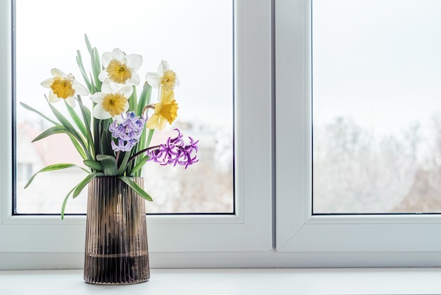 Buquê de primavera de narciso amarelo e jacinto azul e roxo em um vaso de vidro no parapeito da janela
