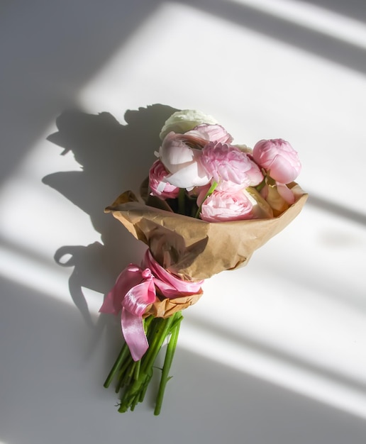 Buquê de ranunculus lindas flores delicadas decoração floral luz solar brilhante e sombras em uma superfície branca