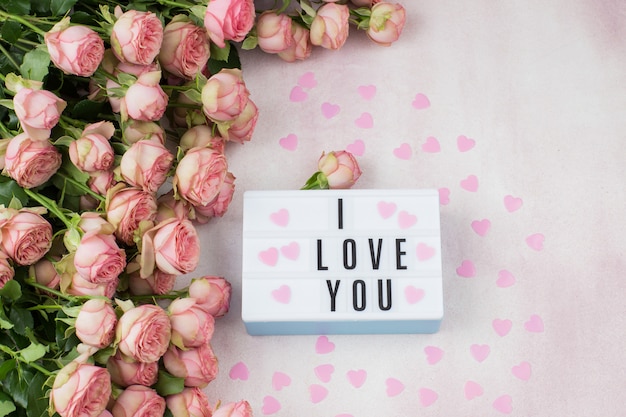 Buquê de rosas, corações rosa e um prato com a inscrição: eu te amo