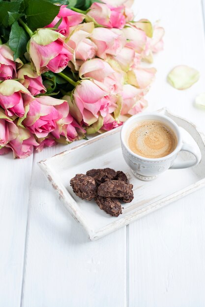 Buquê de rosas em um fundo branco e uma xícara de café com chocolate