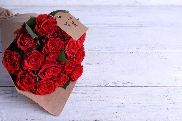 Buquê de rosas vermelhas com etiqueta embrulhada em papel com fundo de madeira