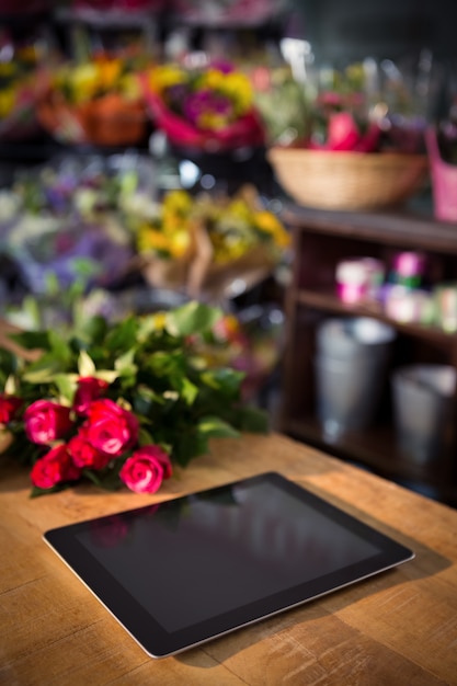 Buquê de rosas vermelhas e tablet digital em cima da mesa de madeira