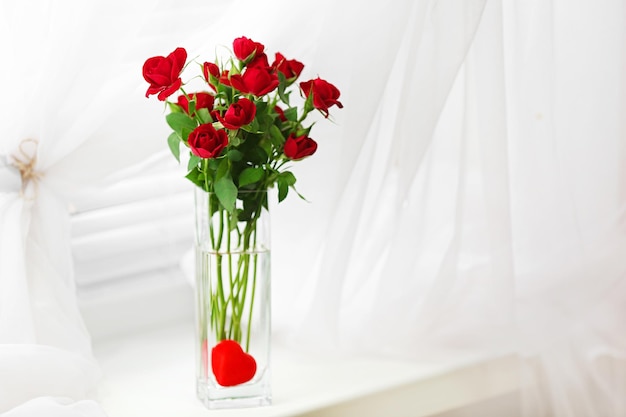 Buquê de rosas vermelhas em vaso de vidro com coração no fundo da janela
