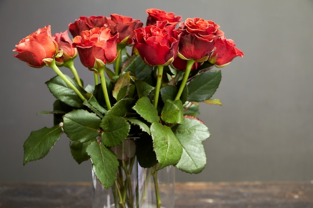 Buquê de rosas vermelho-laranja em um vaso de vidro em uma superfície de madeira escura