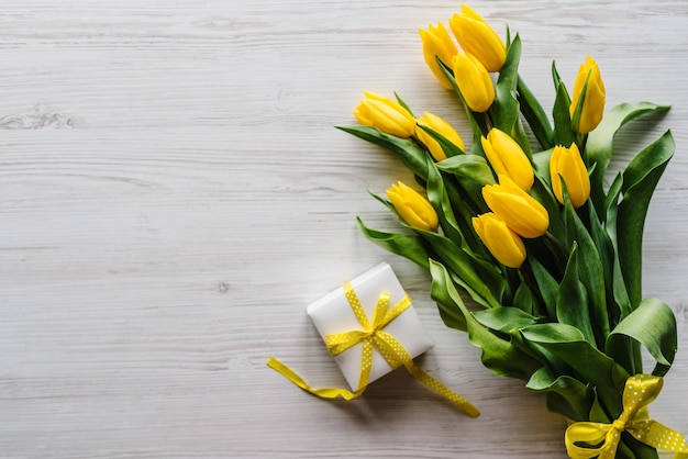 Buquê de tulipas amarelas com caixa de presente em fundo branco de madeira rústica com espaço para mensagem Cartão de férias para dia das mães das mulheres dos namorados aniversário de páscoa vista superior plana lay