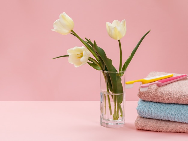 Buquê de tulipas amarelas em um vaso de vidro, toalhas empilhadas e escovas de dente na cor rosa