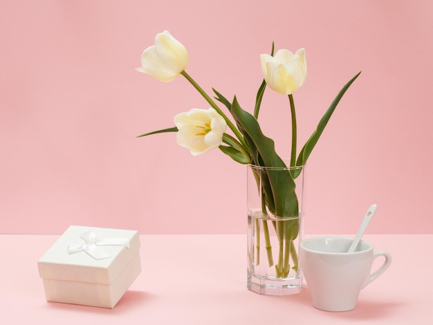 Buquê de tulipas amarelas em vaso de vidro uma caixa de presente e uma xícara de café em um fundo rosa