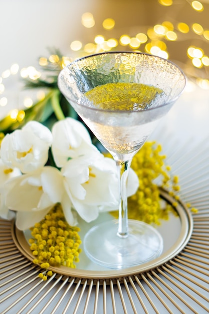 Buquê de tulipas brancas e flores de mimosa na bandeja de espelho com copo de bebida
