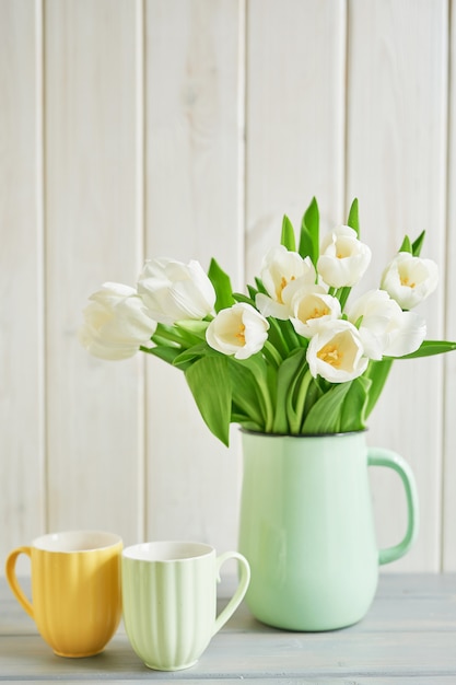 Buquê de tulipas brancas frescas em vaso e duas canecas