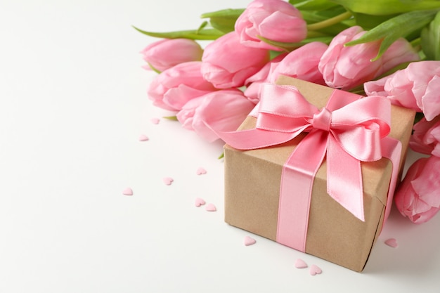 Buquê de tulipas, caixa de presente e pequenas corações em fundo branco, espaço para texto